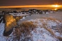The picturesque scenery of the rocky coastline of the Hudson Bay in Churchill, Manitoba during a spectacular winter sunset.