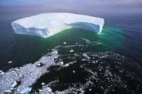 Aerial Photo large free floating iceberg with little ice pieces breaking off and leaving a trail in the deep dark Atlantic Ocean off the Labrador Coast.