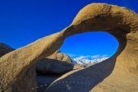 A beautiful scene of the snowcapped Sierra Nevada Mountains framed by Mobius Arch, a rock formation in the Alabama Hills Recreation Area.