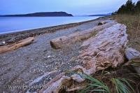 In this beach scene, there is lots of driftwood strewn along the beach in Fillongley Provincial Park, which is part of Denman Island. In the background can be seen Hornby Island and the Strait of Georgia, a major body of water in British Columbia.