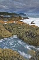 White foamy waves and a rocky coastline are seen along the beautiful scenic West Coast at Cape Palmerston on Northern Vancouver Island. Beautiful blue waters and cloudy skies add to the scenery of Cape Palmerston.