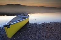 A canoe sits ready to be pushed onto the water on the shores of Lake Monroe as the fog settles over the water at sunset. This picure was taken in Parc national du Mont Tremblant, which is a Provincial Park in Laurentides, Quebec.