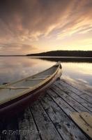 A dramatic sky reflects the sunset on Tuckamore Lake and a Canoe in Main Brook, Newfoundland, Canada.