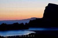 The Castlepoint lagoon in Castlepoint on the North Island of New Zealand is glowing in the light from the sunset as the shape of Castle Rock is outlined.