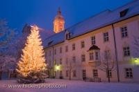 A christmas tree is lit up and glistening in the snow that has fallen outside of the Landratsamt in Neustift, in the city of Freising, Bavaria, Germany. This is a picturesque shot of a quiet winter evening with undisturbed snow on the ground.