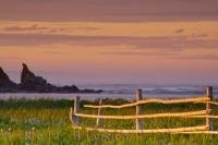 Taken in the town of L'Anse aux Meadows this picture shows the coastal scenery of the Atlantic Ocean and the rugged islands at sunset, as well as a rustic handmade fence in the foreground. This town is on the Northern Peninsula of Newfoundland.