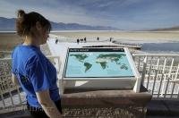 A woman checks out a sign showing the earths lowest points one being the Badwater Basin in Death Valley in California.
