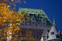 The green roof, and reddish brown exterior of the luxurious Fairmont Le Chateau Frontenac in Old Quebec peers from behind the yellow leaves of a tree.