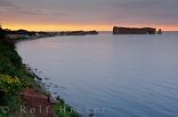 The soft colours of the Gaspesie Sunset reflect in the waters of the Gulf of St Lawrence which gently lap at Perce Rock in the town of Perce, Quebec, Canada.