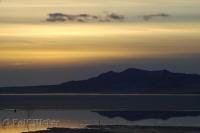The surrounding hills reflect on frozen Great Salt Lake during sunset in Utah, USA.