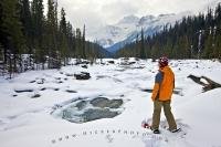 A woman stops and gazes at the stunning winter landscape surrounding the Mistaya River while she is snowshoeing with Mount Sarbach in the background. This is located in Mistaya Canyon off the Icefields Parkway in Banff National Park.
