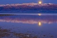 Vivid reflections of the moonrise on Badwater Basin as the moon appears above the Panamint Mountains in Death Valley National Park, California, USA.