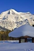 Snow-covered Mount Robson towers above a visitor information kiosk on a blue-sky day in the winter.