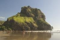 Keeping watch over the beach and tides of Piha Beach, Lion Rock dominates the seascape as people frolic in the surf of the Tasman Sea.