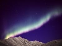 Colorful Aurora borealis, better known as Northern Lights, dancing above lit up mountains  of the Brooks Range during a full moon night with many stars in the sky, Alaska. USA.