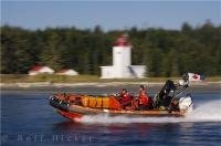The Coast Guard Rescue boat zooms past the Pulteney Point Lighthouse on Malcolm Island, British Columbia, Canada.