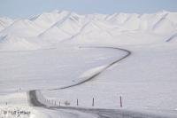 The James Dalton Highway, a gravel road frozen in winter, winds through the snow capped mountains of the Brooks Range in Alaska's arctic.