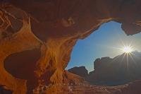 The curve of Arch Rock frames the sun as it sits atop a series of formations in the Valley of Fire State Park, Nevada, USA.