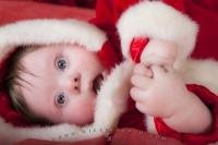 A cute baby dressed in a santa outfit lying on his side with hands together.