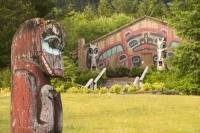 A old Totem Pole in front of a long house in Saxman Totem Park in Ketchikan.