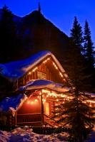 A real winter scene of a cabin covered with fresh snow lit up by decorative lights which give the cabin a sense of coziness and warmth despite the cold surroundings of winter.