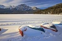 A row of snow covered canoes along the shoreline of Pyramid Lake near the town of Jasper in Jasper National Park during winter.