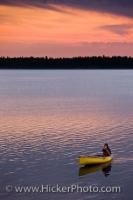 A glorious sunset lights the evening sky over Lake Audy in Riding Mountain National Park, a lush tract of wilderness featuring lakes and forests, as a paddler returns to shore in a canoe before nightfall.