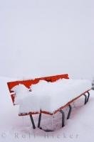 A snowstorm late in the season covers this red park bench with mounds of snow in the Oberalppass near Andermatt, Switzerland.