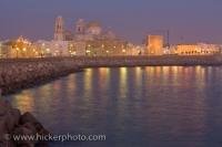 The evening street lights along the waterfront in the City of Cadiz sends colorful streams of light across the water surface as dusk falls over the city which is situated along the Atlantic Ocean coast in Andalusia, Spain - a popular travel destination.
