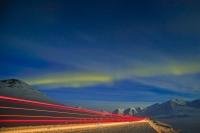 The arctic landscape is lit by the aurora borealis and a passing truck along the James Dalton Highway, Alaska, USA.