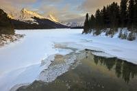 A beautiful scenic view of the partially frozen Maligne River and Maligne Lake leading back towards the landscape of the snow-capped mountains during winter in Jasper National Park.