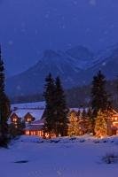 This wintry snow covered night scene that is illuminated and surrounded by trees and decorated trees is the Post Hotel located on the banks of the Pipestone River in Banff National Park in the Canadian Rocky Mountains, Alberta.